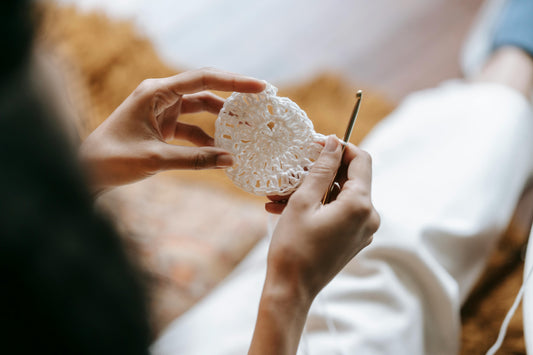 Close-up of hands crocheting a white round motif with a gold hook