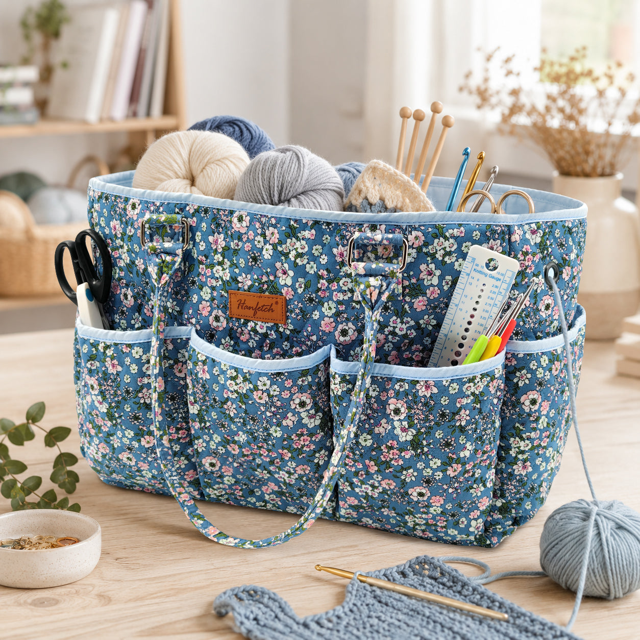 Blue floral quilted yarn tote, shown holding yarn with hooks and scissors in the outer pockets