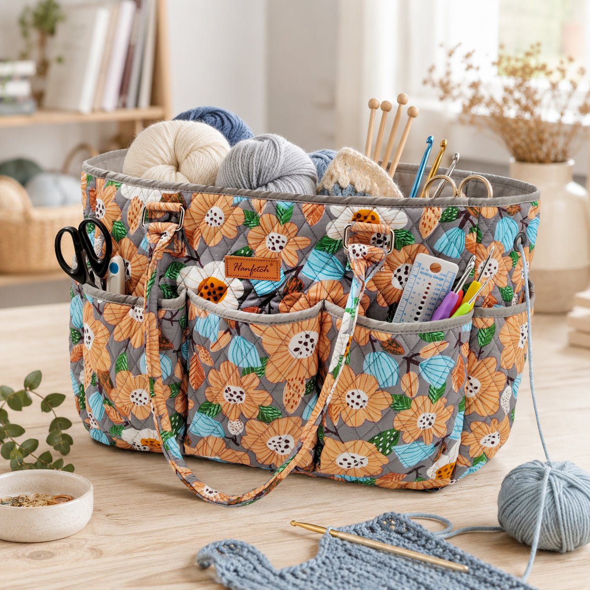 Grey floral quilted yarn tote with orange flowers, shown holding yarn and tools in the outer pockets