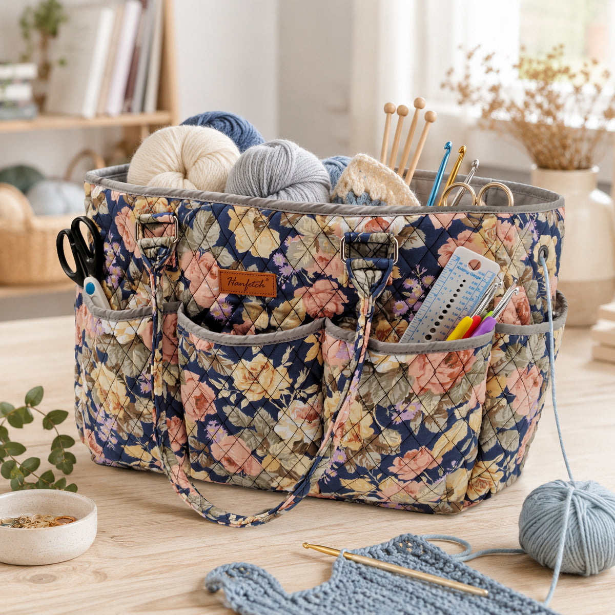 Peony-print quilted yarn tote with pink and cream flowers, shown holding yarn and crochet tools