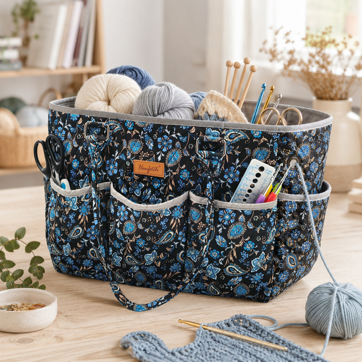 Blue paisley quilted yarn tote on a craft table, shown holding yarn, knitting needles and crochet tools
