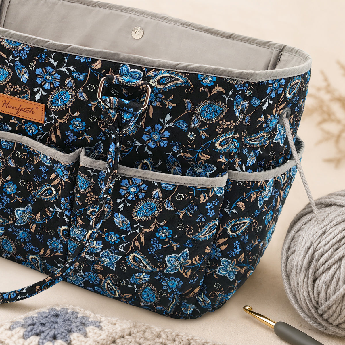 Close-up of the quilted tote showing front pockets, a yarn-feed grommet and the snap closure